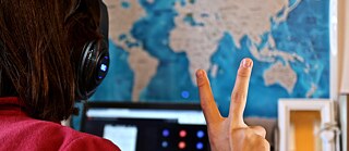 Un(e) adolescente avec des écouteurs devant un écran montre le signe de la victoire.