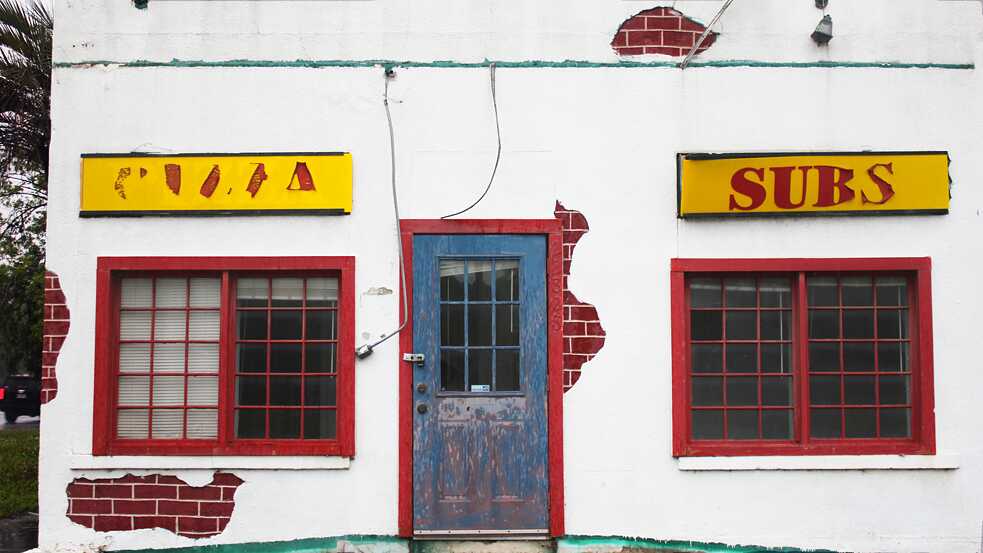 The exterior of an abandoned restaurant selling pizza and subs