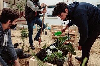 Des élèves plantent un pot de fleurs fait de palettes.