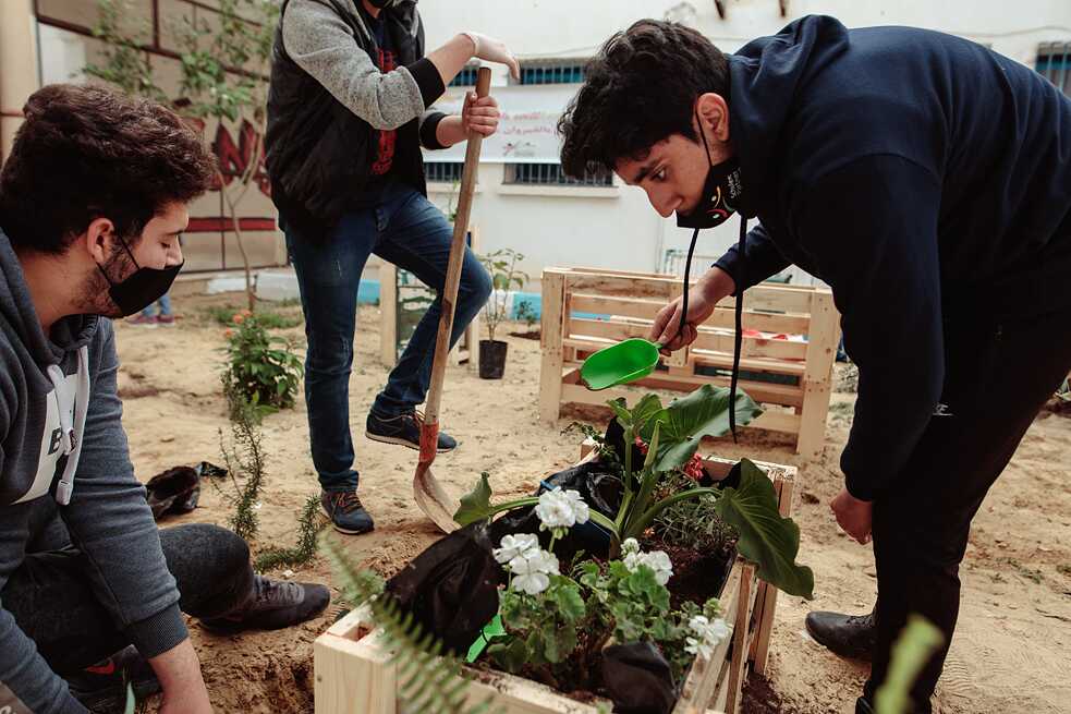 Des élèves plantent un pot de fleurs fait de palettes.