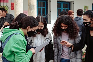Les élèves sont regroupés en demi-cercle et se parlent. Ils ont une feuille de papier dans la main.
