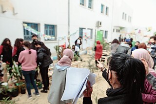 Une femme vue de dos montre la cour de l'école, où de nombreuses personnes font des activités de jardinage.