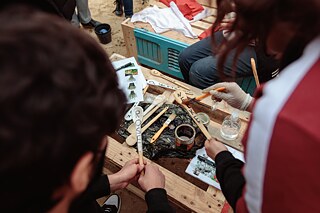 Les mains des élèves vernissent des cuillères en bois avec les noms de plantes.