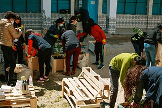Les élèves plantent des pots de fleurs dans la cour de l'école. Au milieu, on voit un banc fait de palettes.