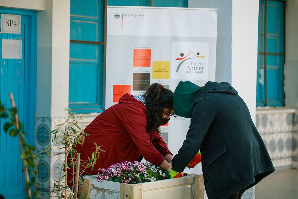 Des élèves plantent un pot de fleurs fait de palettes.