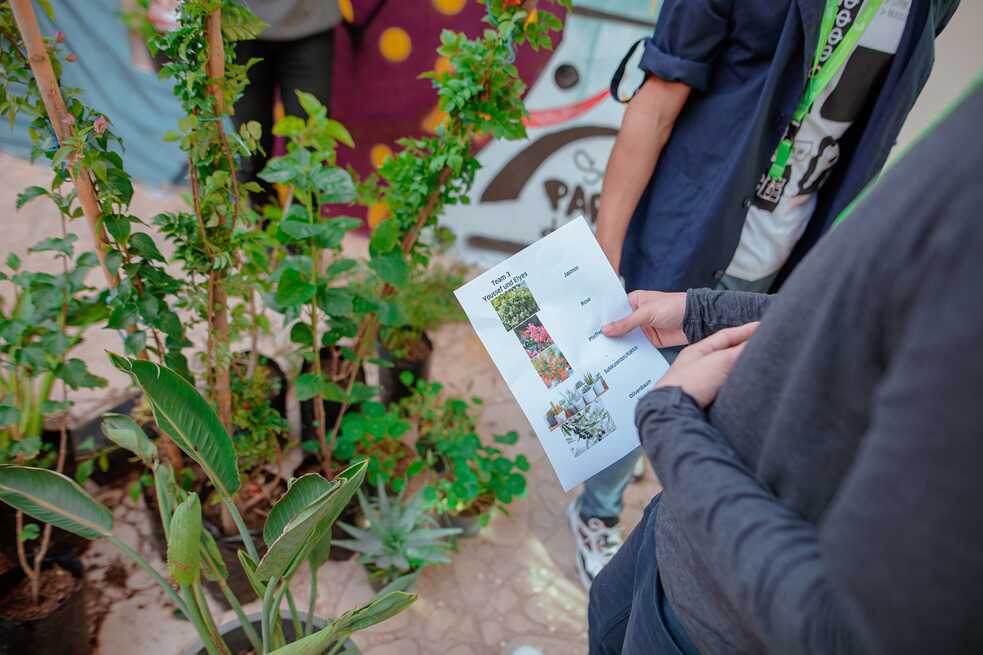 Mains des élèves qui tiennent une liste de noms des plantes à côté de nombreux types de plantes.
