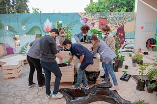 Jugendliche bepflanzen Blumentöpfe aus Paletten auf dem Schulhof vor Graffiti.