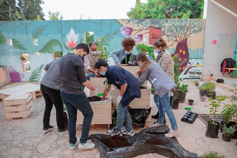 Les élèves plantent des pots de fleurs à partir de palettes dans la cour de l'école devant un mur couvert de graffitis.