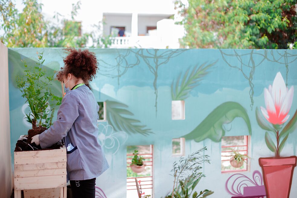 Une jeune élève sort une plante de son emballage. Elle se tient devant un mur couvert de graffitis.