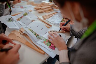Hände von Jugendlichen, die Holzlöffel mit Pflanzennamen  beschriften.
