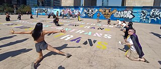 Eine Gruppe von Demonstrierender auf einem Platz, auf dem das Wort „Juntrans“ mehrfach gemalt ist