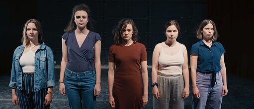 Eine Reihe von jungen Frauen vor einem dunklen Hintergrund sehen in die Kamera