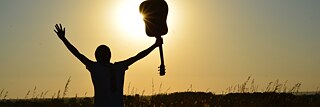 Silhouette of a man in a field exultantly holding a guitar up in the air 
