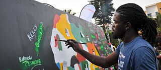 A Ugandan artist painting a mural, on which the shape of Africa is drawn and filled in with colour. 