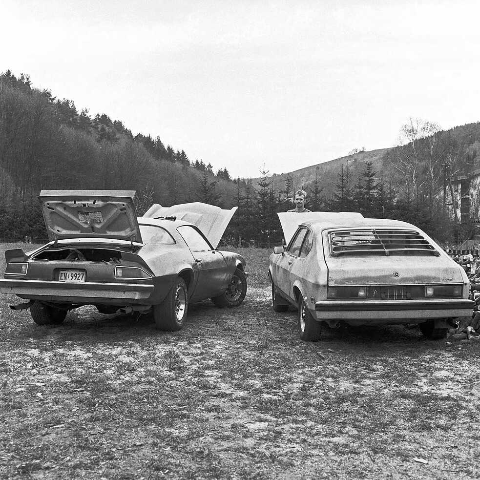 A man standing in front of two cars in a field in Neumühle, Germany