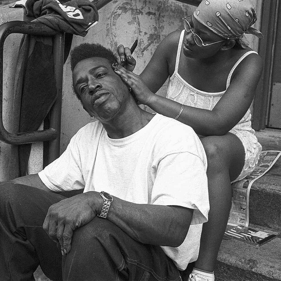 A woman braiding a man’s hair in the street