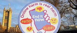 A large badge from the UK charity Girlguiding with the words “Online harm is real harm. End it now” printed onto the material.