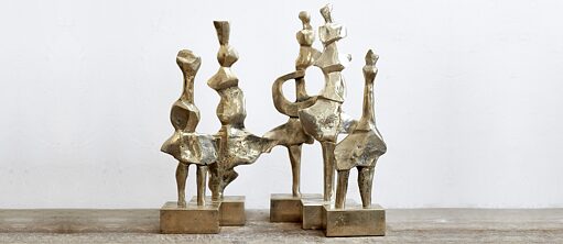 Arka planı beyaz bir duvar olan bir fotoğraf. Ön planda ahşap bir zemin üzerinde beş bronz renkli heykel bulunmaktadır. Kaydırılarak arka arkaya  ve yan yana yerleştirilmiş olan heykellerin tümü aynı malzemeden yapılmış olan kendi bronz kaideleriyle bağlantılıdır. Heykeller soyut insan ve hayvan figürlerini andırmaktadır.