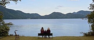 Drei Personen sitzen auf einer Bank vor einem See