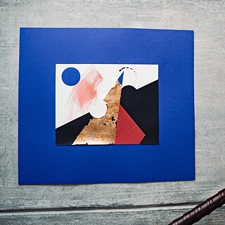 Eine Nahaufnahme eines Kunstwerks, das an einer grauen Wand angebracht ist. Das Kunstwerk ist leuchtend blau und weist in der Mitte Formen in Schwarz, Weiß, Rot, Rosa und Blau auf – ein Kunstwerk aus einer der Ausstellungen des Goethe-Instituts Irland.
