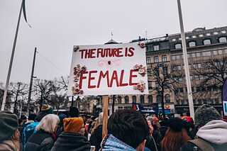 Eine junge Frau hält ein Plakat mit der Ausschrift „The Future is Female“ bei einer Kundgebung.
