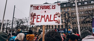 Девушка держит плакат «Будущее за женщинами» на митинге