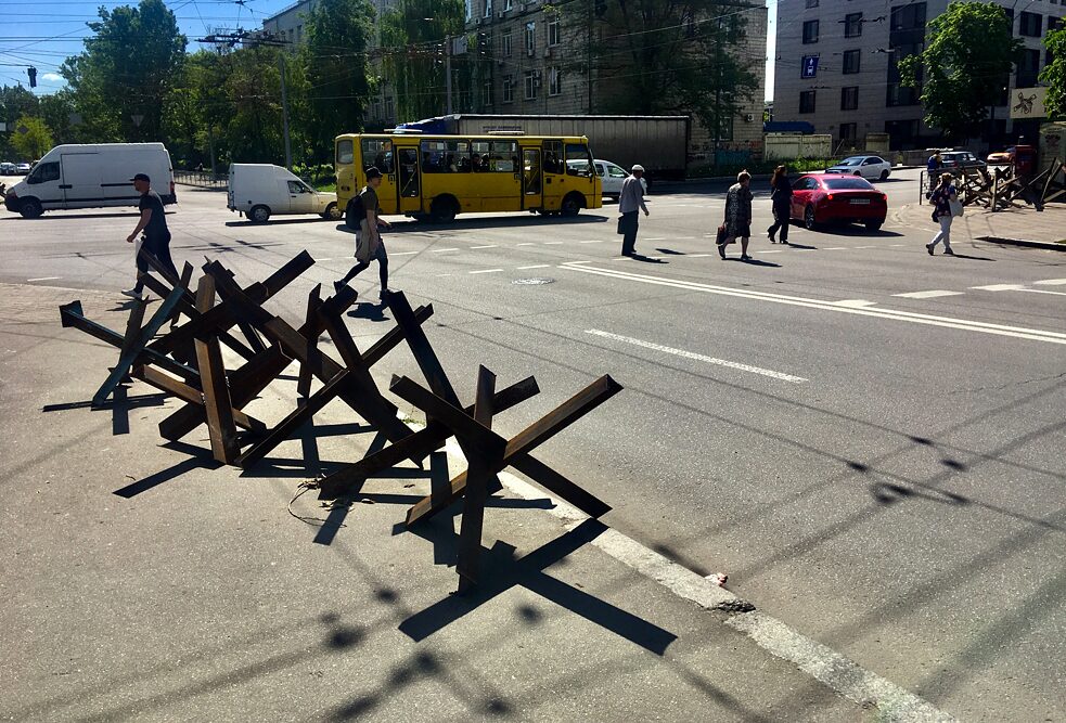 An vielen Straßenkreuzungen Kyjiws stehen noch Panzersperren bereit, falls die russischen Truppen noch einmal versuchen werden, die ukrainische Hauptstadt zu stürmen. Aktuell schützen sie vor allem den Fußweg vor wild parkenden Autos.