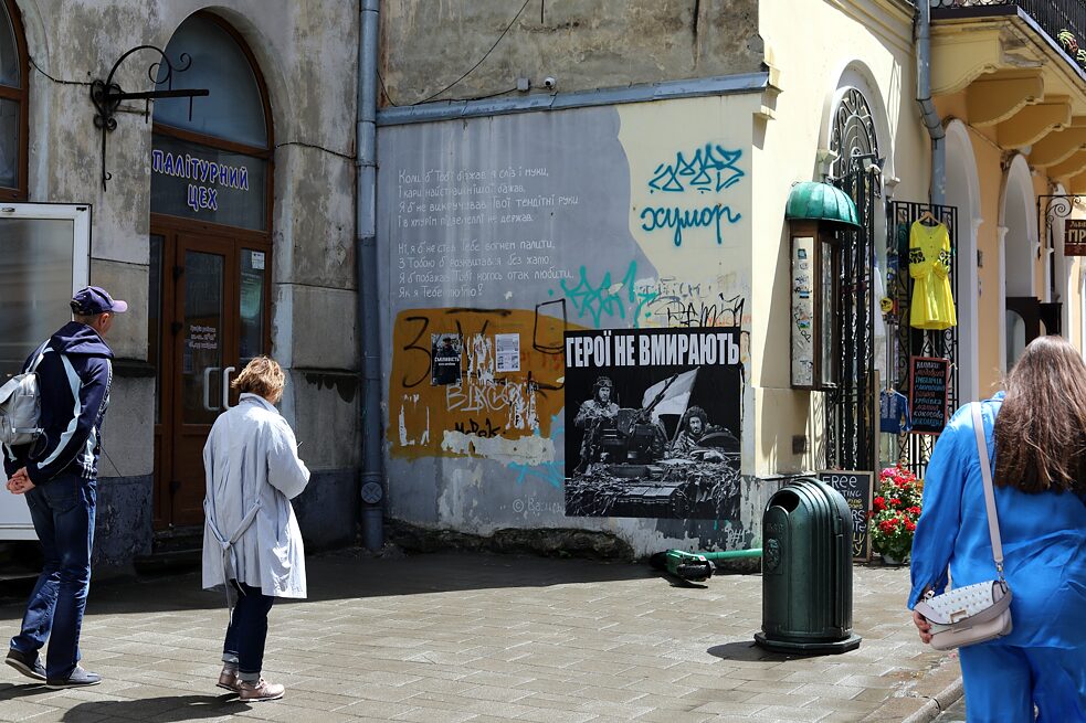 „Helden sterben nicht!“: In der Lwiwer Altstadt sind zahlreiche Plakate und Graffiti über den Krieg zu finden. In den Souvenirläden gibt es dazu Merchandising und traditionelle, folkloristisch bestickte Kleidungsstücke.