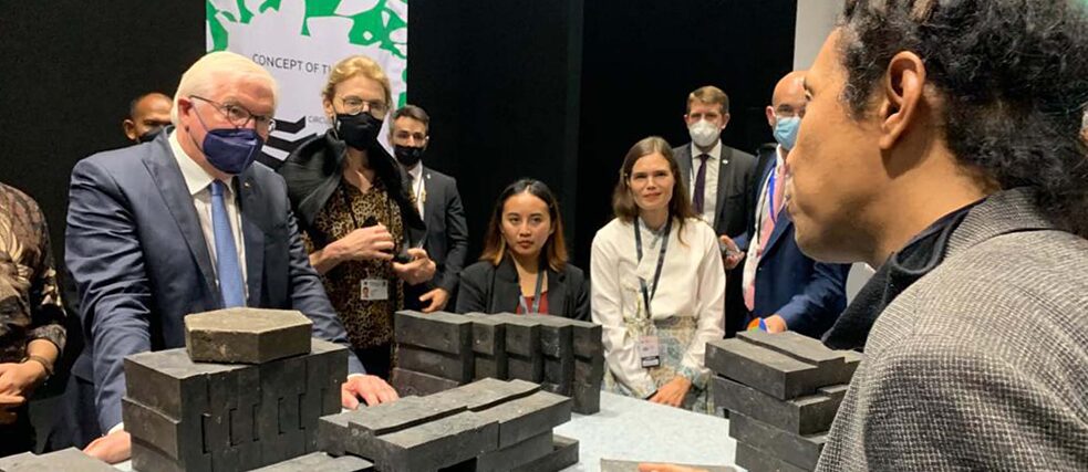 Bundespräsident Steinmeier betrachtet Steine aus gepresstem Plastik, die für den Bau des “Monumen Antroposen” verwendet werden.