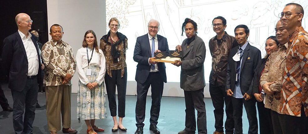 Bundespräsident Steinmeier erhält von den Kurator*innen einen Stein als Präsent überreicht.