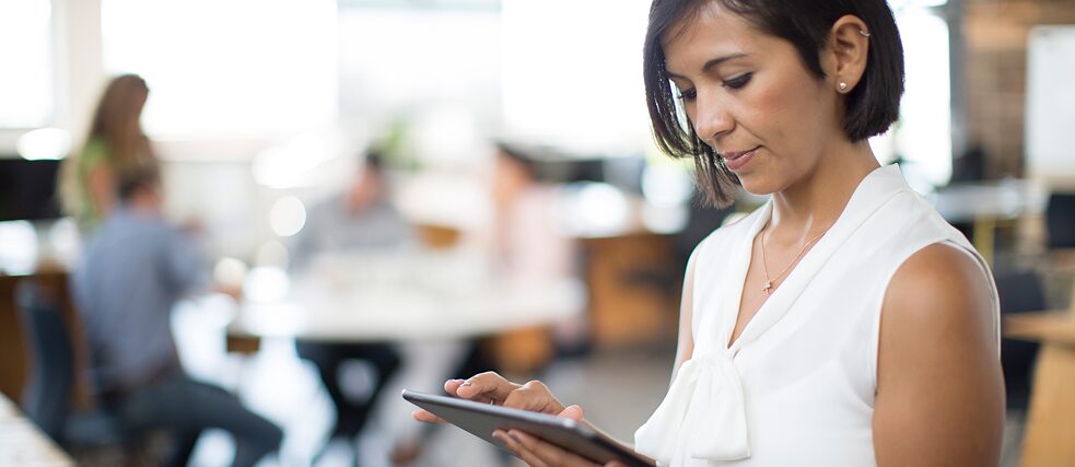 Mediendidaktik Eine Geschäftsfrau in einem modernen Büro tippt etwas in das Tablet.