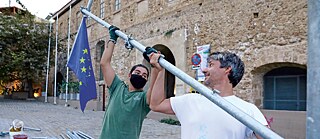 Zwei Männer stemmen einen Fahnenmast, an dem eine Europafahne hängt
