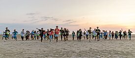 Viele Kinder laufen bei Sonnenuntergang am Strand auf die Kamera zu 