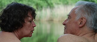 Η εικόνα δείχνει ένα ηλικιωμένο, μάλλον γυμνό ζευγάρι σε πορτραίτο. Τα δύο άτομα κάθονται με την πλάτη τους προς τον θεατή και κοιτάζονται μεταξύ τους. Η γυναίκα, που κάθεται στα αριστερά, έχει καστανά, σγουρά μαλλιά μέχρι το ύψος του πηγουνιού. Ο άντρας, στα δεξιά, έχει γκρίζα κοντά μαλλιά και την κοιτάζει με ενδιαφέρον. Το πράσινο θολό φόντο υποδηλώνει ότι βρίσκονται στη φύση.