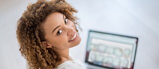 Junge lächelnde Dame am Laptop schaut über Schulter zu dir hin. 