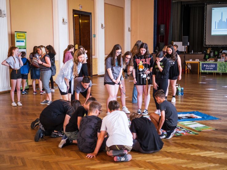 Skupina studentů se sklání nad úkolem na podlaze.