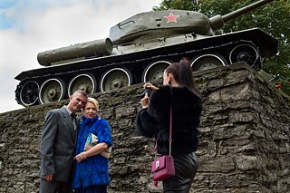 Eine junge Frau fotografiert ein schick aussehendes Paar vor einem sowjetischen Panzer.
