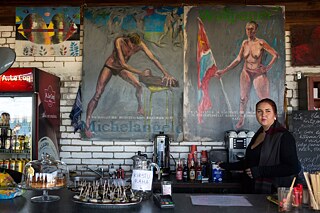 Eine junge Frau steht hinter der Theke einer Bar. 