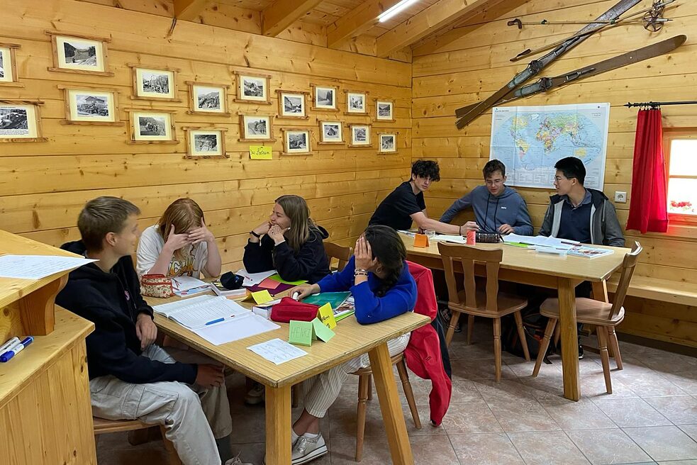 Jugendliche in einer Almhütte, vor ihnen lieben Lernmaterialien auf den Tischen.
