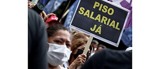 Eine Demonstrantin hält ein Schild hoch mit der Aufschrift „Mindestlohn jetzt“, während eines Protestes von Lehrer*innen des öffentlichen Bildungssystems in Brasilien.