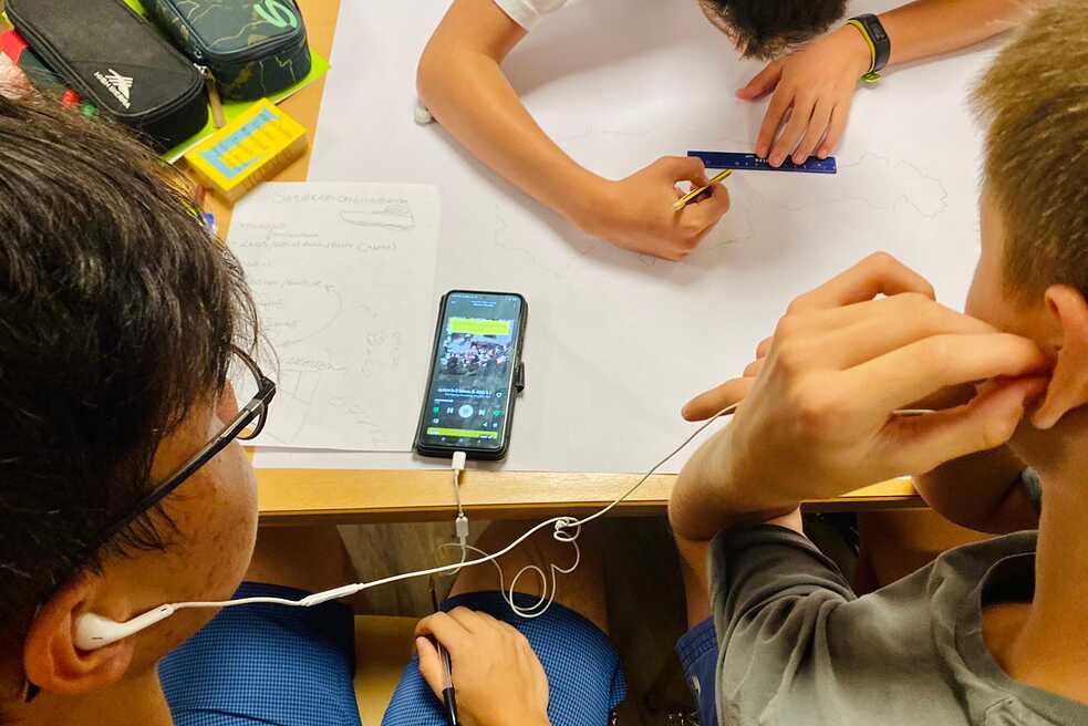 Jugendliche sitzen an einem Tisch und hören etwas vom Handy.