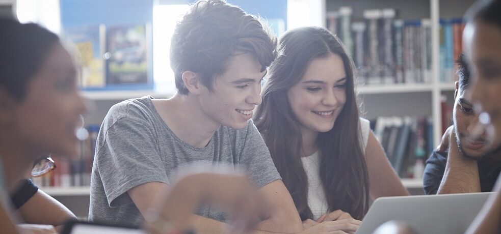 Mehrere Schüler*innen arbeiten mit Tablets und Laptop in der Bibliothek.