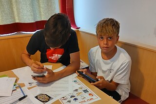 Jugendliche sitzen an einem Tisch, sie haben Arbeitsblätter vor sich liegen.