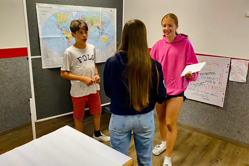 Jugendliche stehen vor einer Pinnwand.