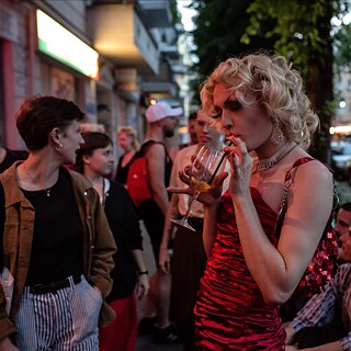 Persone in piedi fuori da un locale berlinese; una persona beve un cocktail.