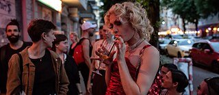 People are standing outside a Berlin club, one person is drinking a cocktail.