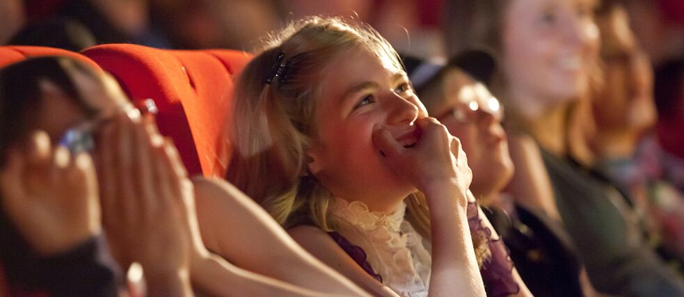 Mitglieder einer Kinderjury sitzen bei einem Kinderfilmfestival im Zuschauerraum und amüsieren sich über einen Filmbeitrag.