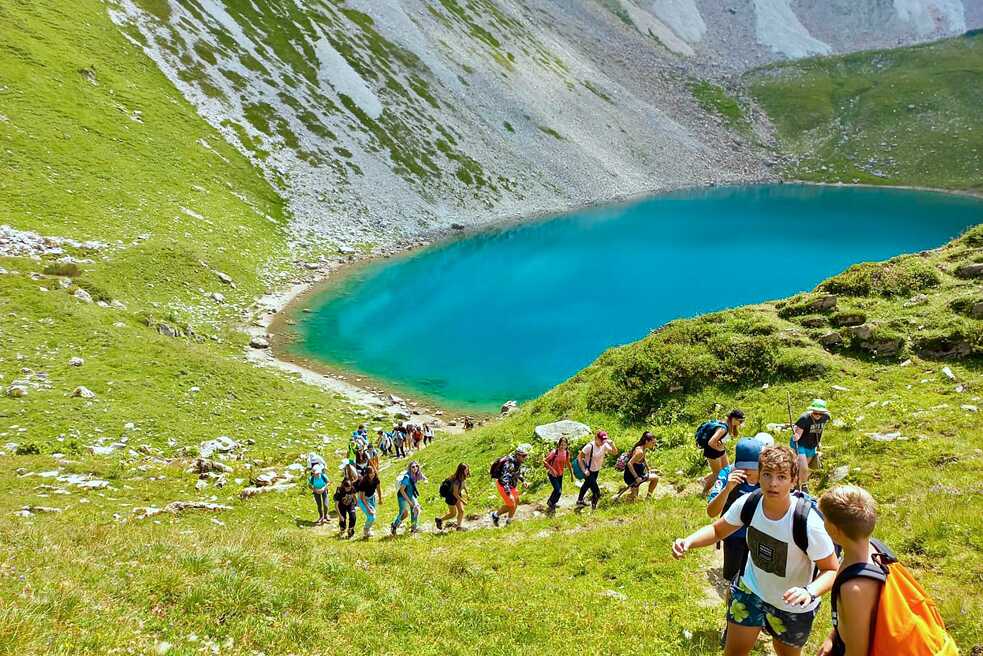 Jugendliche wandern in den Bergen. Im Hintergrund ein kleiner See.