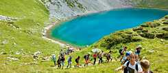 Jugendliche wandern in den Bergen. Im Hintergrund ein kleiner See.
