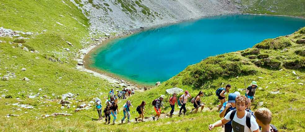 Jugendliche wandern in den Bergen. Im Hintergrund ein kleiner See.